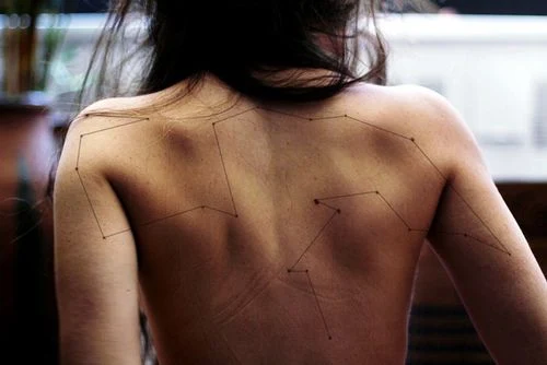 chica desnuda de espaldas con el tatuaje de una constelacion 