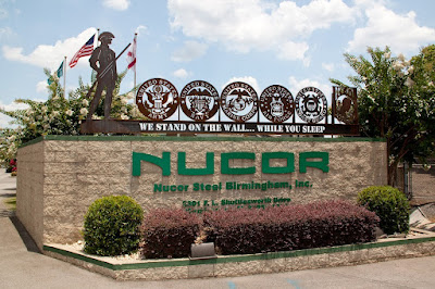 The sign for Nucor Steel. There are shrubs growing around it.
