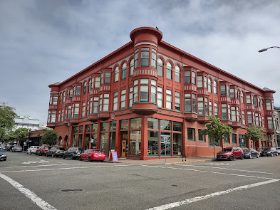 Photo of a late 19th / early 20th c. building in Eureka, CA. It is ochre colored and rectangular. It has three storeys, with circular bays at the corners on the second and third floors, four window bays on the visible short side and six bays on the visible long side. All of the bays are on the second and third floors only.