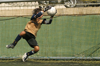 Javier Arjona está blocando el balón en el aire, haciendo una parada espectacular.