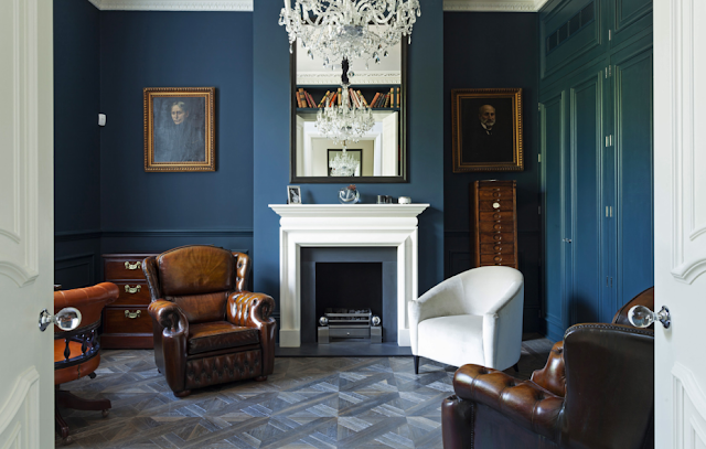 Blue library in a suburban London home with leaher club chairs, carved crown moulding, parquet wood floors, decorative wall moulding and paneling