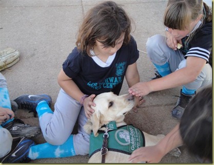 Reyna is laying on the ground as three teamates pet Reyna.  One of the girls has her hand over Reyna's nose, and Reyna is not licking her.  Good girl, Reyna!
