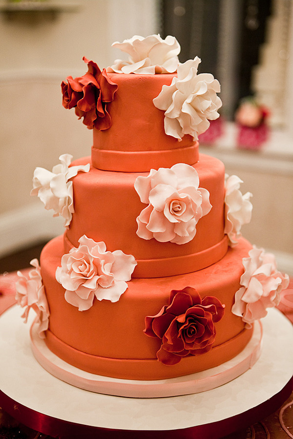 Three tier deep orange round wedding cake with white flowers and a white