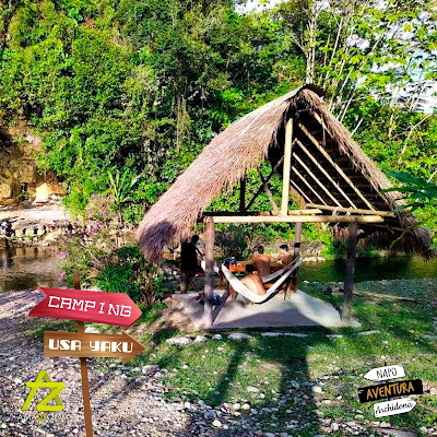 Una acogedora cabaña de madera con hamacas frente a un río cristalino en el corazón del bosque amazónico, donde turistas disfrutan de momentos de relajación y conexión con la naturaleza.