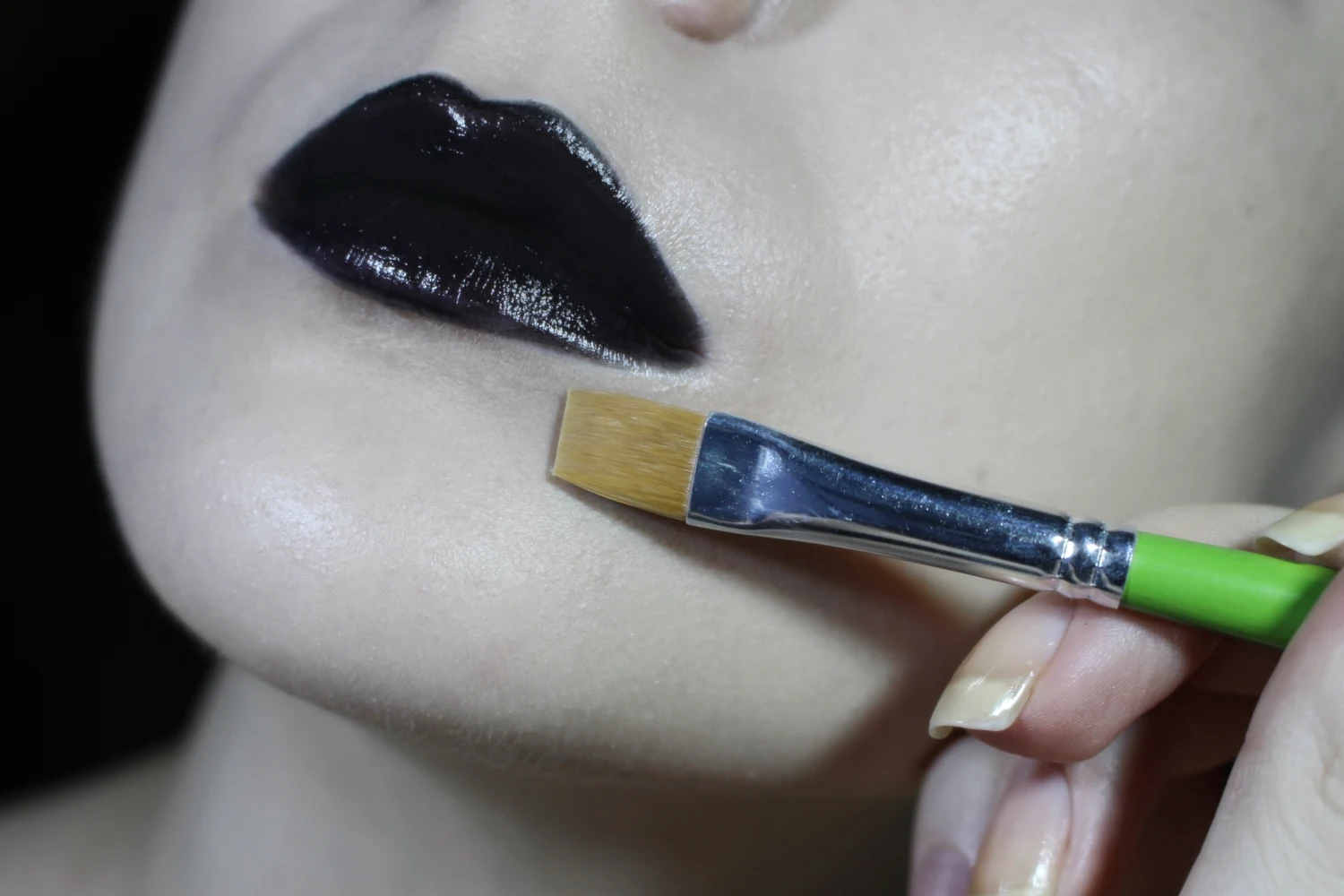 close-up of a pale woman's face and a process of black lipstick application