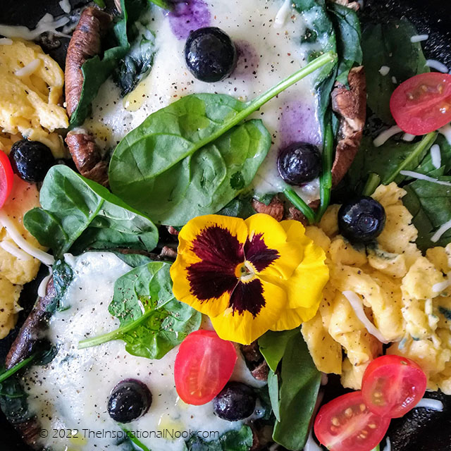 Portobello mushrooms steaks with scrambled eggs, spinach leaves, melted cheese, blueberries, cherry tomatoes and yellow pansies
