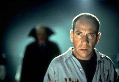 "The Night Flier" (1997) horror movie still where Miguel Ferrer stands in the middle of an airport full of bodies with a vampire killer right behind him