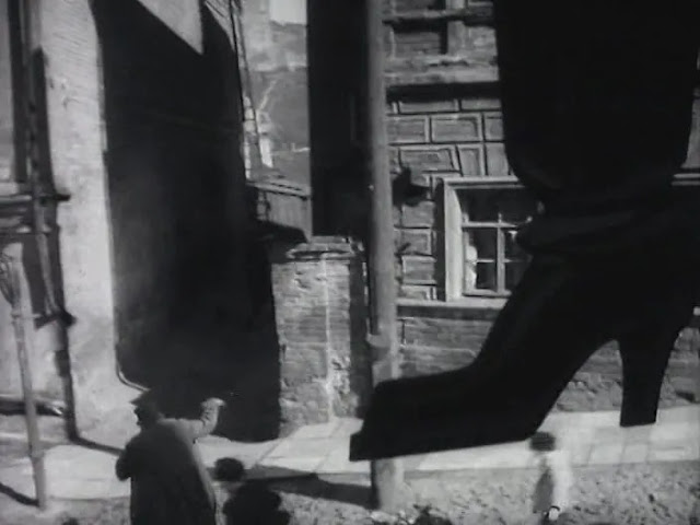 монохромный кадр из фильма где человек забегает в переулок меж двух зданий