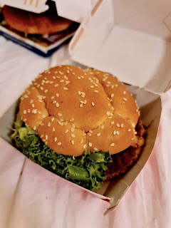 A photo of a burger consisting of dark brown circular patties green lettuce white cheese and purple red onions in a slightly stained red golden brown circular bun on a bright background