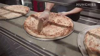 A pizza is being sliced equally in the open kitchen of a pizza restaurant.