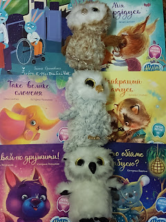 Trzy pluszowe sówki stojące jedna na drugiej obok nich książki dla dzieci po ukraińsku.