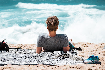 Hombre tumbado en la playa en una toalla con sus pertenencia al lado