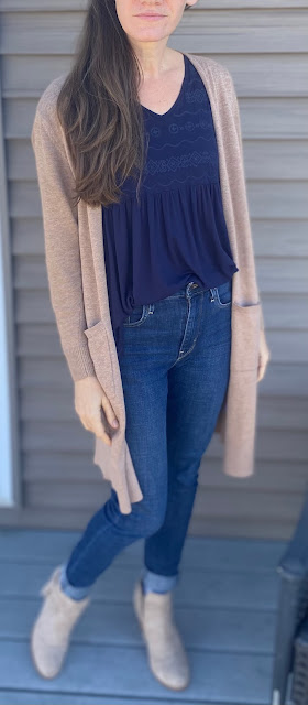 woman in tan cardigan, navy shirt, jeans, and booties