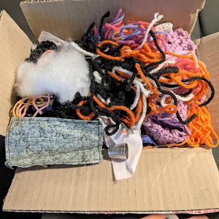 A small cardboard box overflowing with yarn, fabric, stuffing and string.