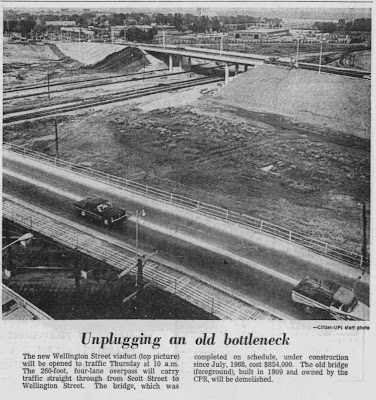 Newspaper clipping of a photo and caption, presumably taken from the roof of the City Centre building, with a caption headline 'Unplugging an old bottleneck', showing the ramshackle Wellington St viaduct in the foreground and the new Scott-Albert bridge over the railway tracks in the background, the two structures separated by a vacant field.