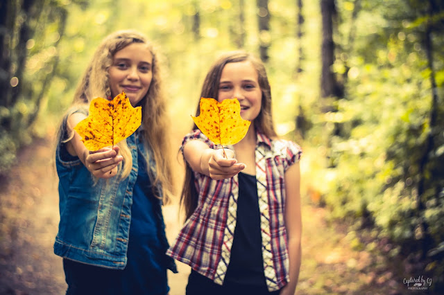 portrait two sisters holding yellow fall leaves in the woods