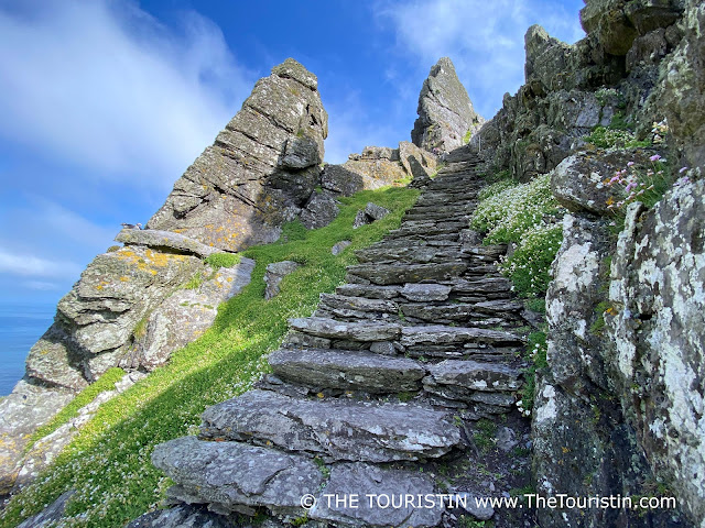 A steep stone staircase leads up through a craggy mountainscape under a bright blue sky.