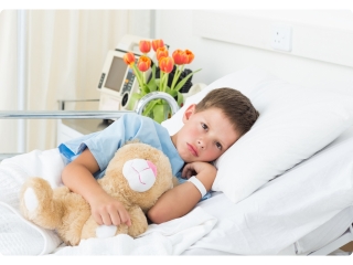 A young boy lying in a hospital bed holds his teddy bear close, seeking comfort during illness.