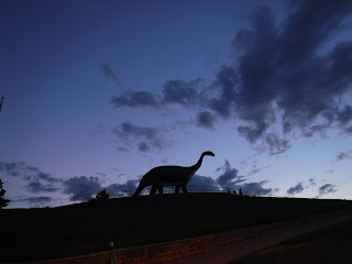 the silhouette of a huge concrete brachiosaurus sits against a darkening sky in Rapid City, South Dakota