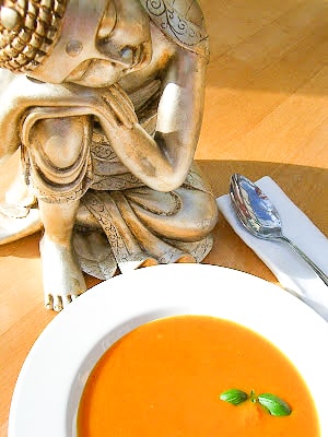 butternut squash and orange soup in a white bowl beside a buddha.