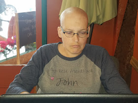 A bald woman sitting in front of an open laptop, looking at the screen in concentration.