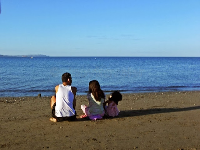 nice view of a father mother and daughter sitting by the beach looking out to the sea all under the wash of early morning sun at San Jose Occidental Mindoro