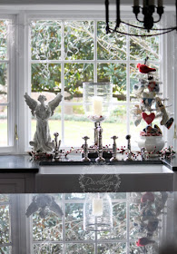 Kitchen window at Christmas with glitter angel, candles and tinsel tree.