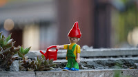 A Lego-man toy with a red watering can in a planter.