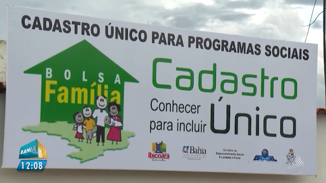 Foto da placa de onde faz cadastro para programas sociais, com desenho do bolsa familia de cor verde e amarela e uma familia e logos do municipio de demais entidades do governo