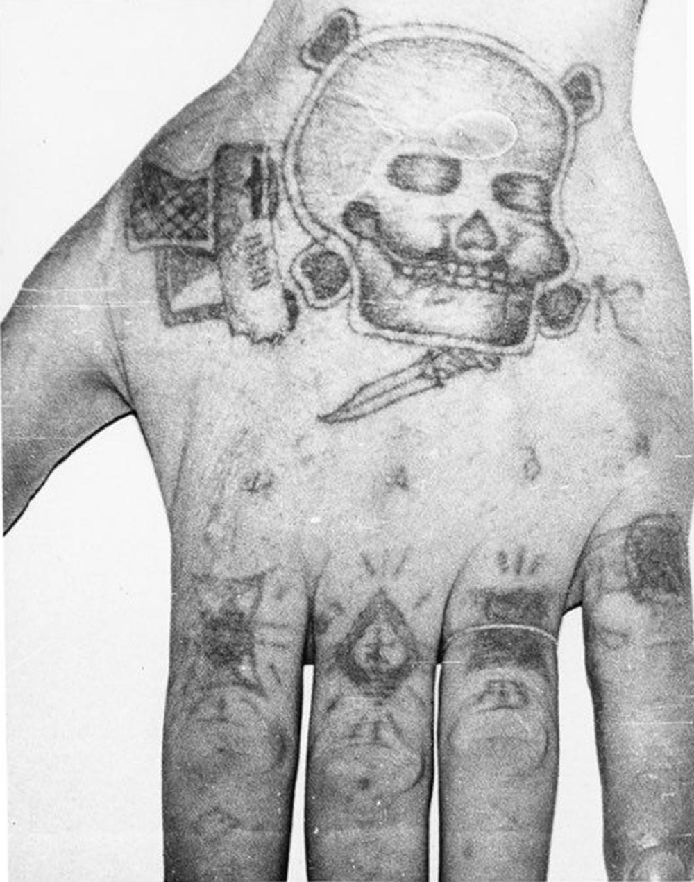 Text across the knuckes reads NADYA (womans name). The 'ring' on the forefinger stands for 'Rely on no one but yourself', a 'patsan' one of the most privileged inmates VTK. Middle finger 'the thieves cross' of a pickpocket. Third finger: 'I served my time in full', 'From start to finish', 'Went without parole', the prisoner served his complete sentence with no remission for working with the system. Little finger 'The dark life' the bearer spent a lot of time in a punishment cell. The skull and crossbones, gun, knife and letter 'K'[iller] denote a murderer.