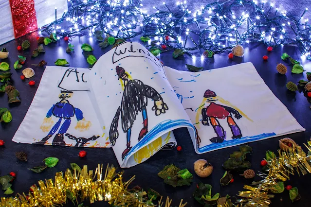 A white tea towel folded in half with a child's drawings of people visible on it