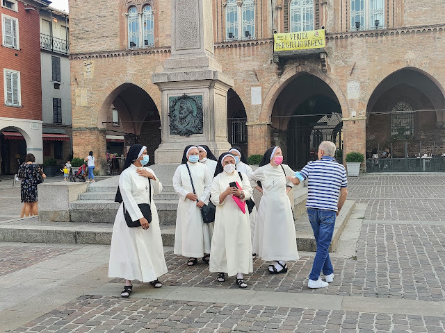 Five nuns in habits and masks in the main piazza.