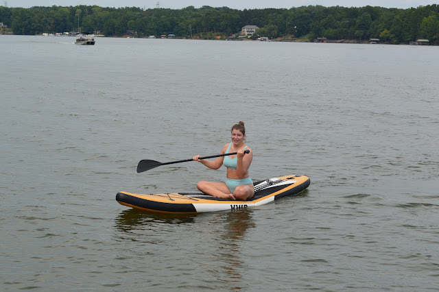 Elizabeth smiling at the camera while sitting on the paddle board.