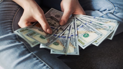 A female counting dollar bills over her blue jeans folded legs.