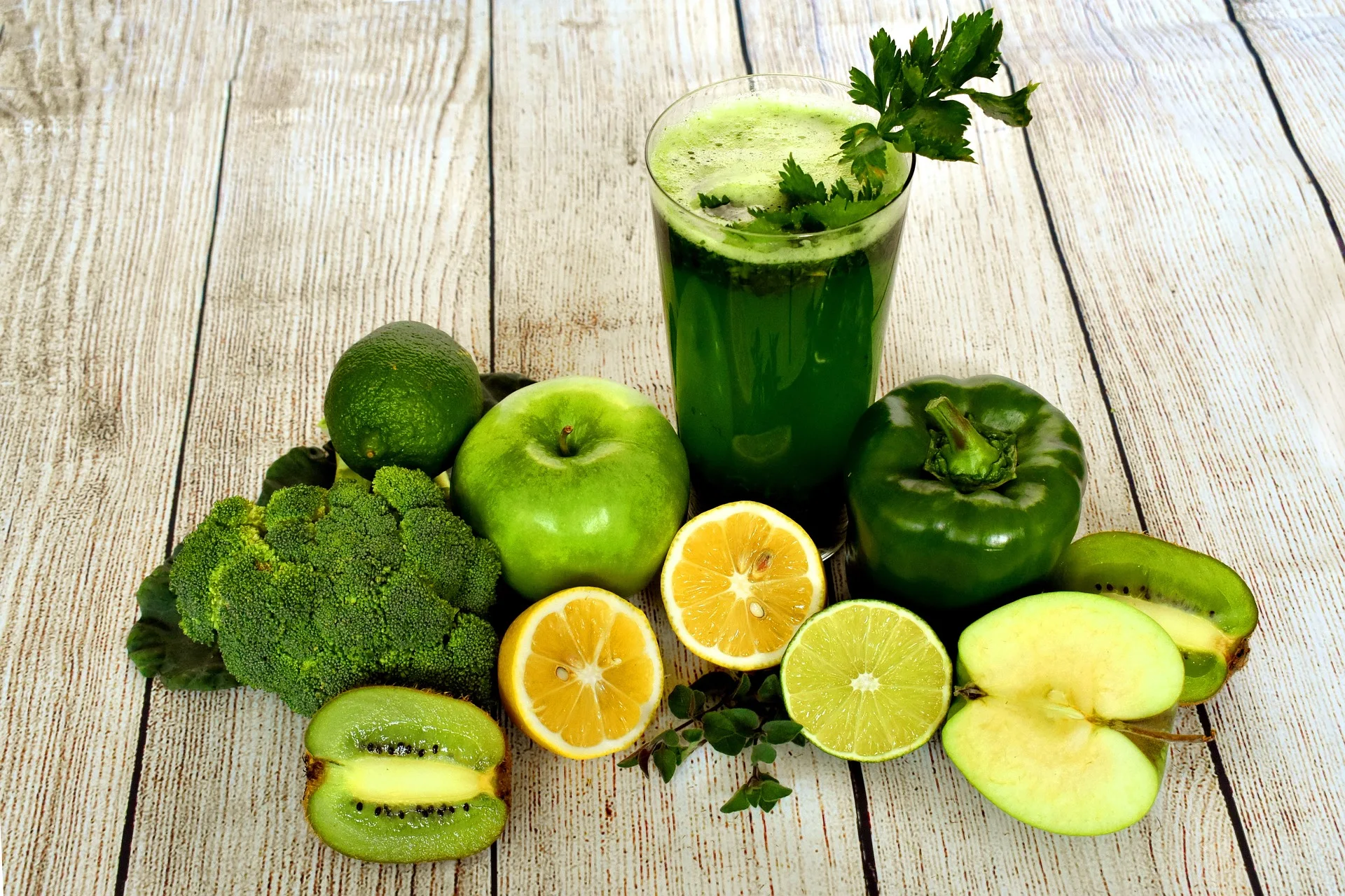 A selection of fresh green fruits and vegetables arranged alongside a glass filled with a nutritious green smoothie, highlighting the importance of a balanced diet for physical health.