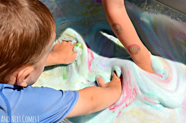 Toddler and preschooler playing in a tie dye sensory bin with soap foam