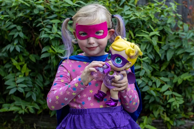 a young girl dressed as a superhero giving super cute little babies doll her bottle