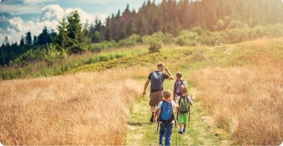 Three boys wearing backs packs, hiking through the field with their father