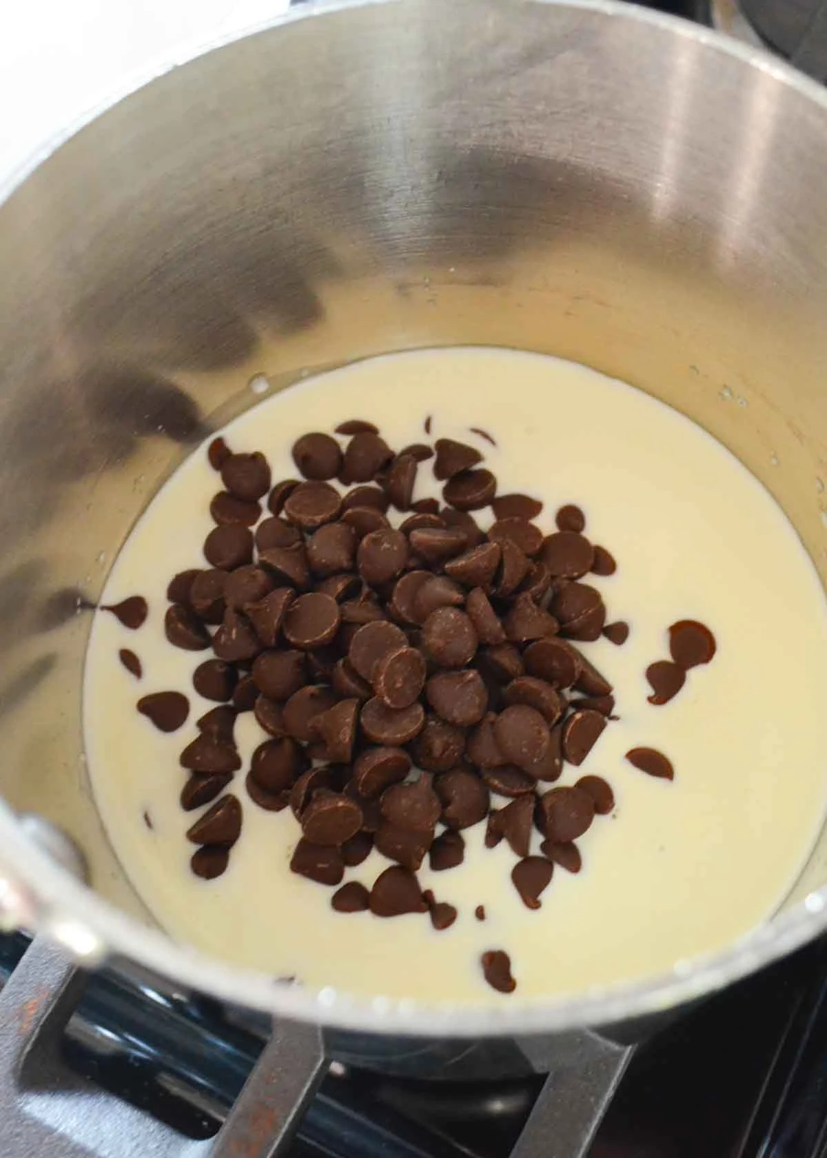 Heavy Cream and Chocolate Chips in a small stainless steel pot on a gas stove top.