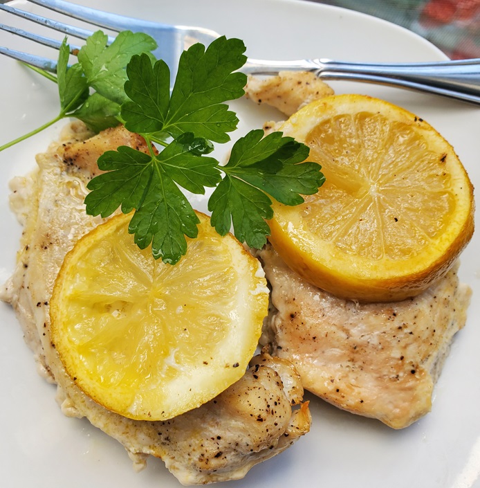 lemon chicken unbreaded on a white plate with herbs and lemon slices