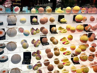 Three glass rectangular shelves filled with colourful spherical bath bombs on a bright background 