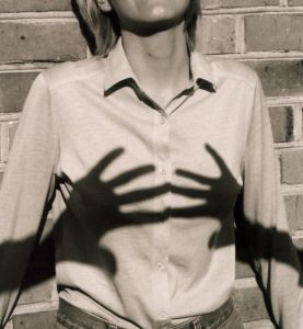 Photo en noir et blanc représentant l'ombre de deux mains sur la poitrine d'une femme.