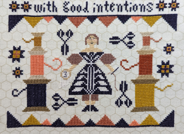 Good Intentions by Kathy Barrick cross stitch, words read I myself am made entirely of flaws stitched together with good intentions, a lady holding an embroidery hoop and needle. There are scissor and star motifs and stacks of thread spools.