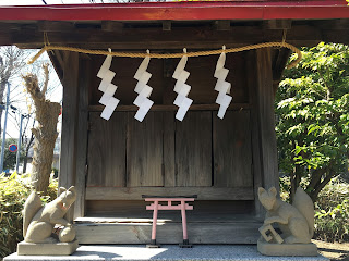 A photo of two foxes or inari guarding a small shrine in Tokyo with a red torii gate in the centre and shide white paper hanging from a rope