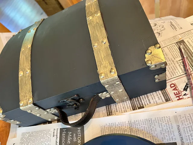 Photo of gold metallic paint highlights being added to a wooden suitcase.