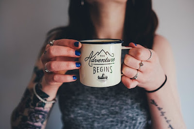 woman holds a cup that reads adventure begins 