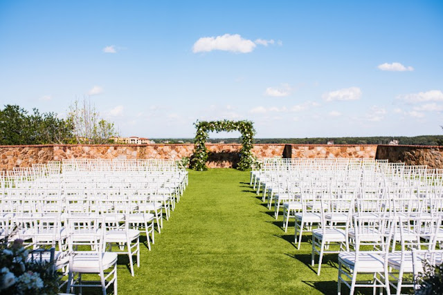 wide angle view of bella collina wedding reception with white chairs and greenery arch