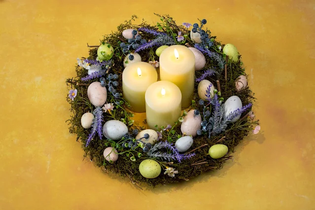 An Easter wreath with moss, eggs and artificial flowers with 3 battery operated column candles in the middle