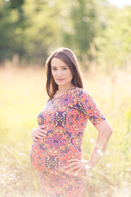 She stands in a glowing field of grass and wildflowers lit by the setting sun.  She's wearing a beautifully patterned coral colored dress, and at 37-weeks, her belly is full and round and beautiful.