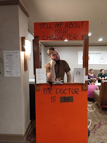 John, a dark haired and bearded man, standing in the Tell Me About Your Character booth at Big Bad Con